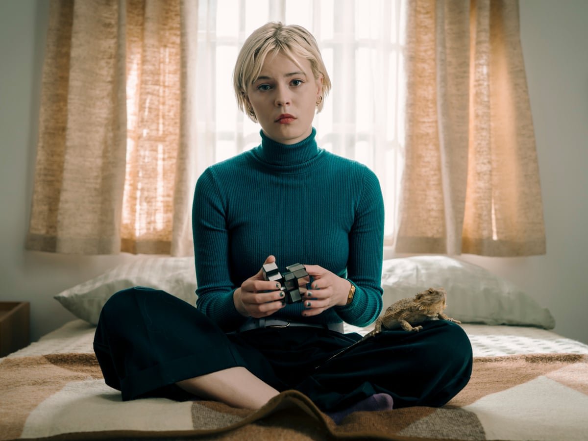 Person sitting on a bed holding a puzzle cube with a lizard beside them