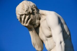 Stone statue with its face resting in one hand against a blue sky