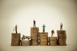 Miniature people standing on stacks of coins at different heights