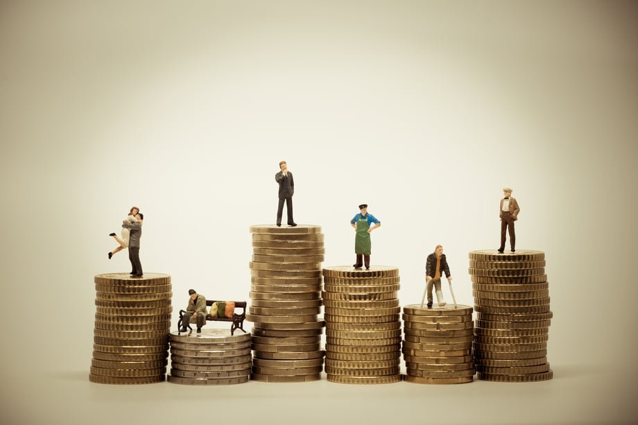 Miniature people standing on stacks of coins at different heights
