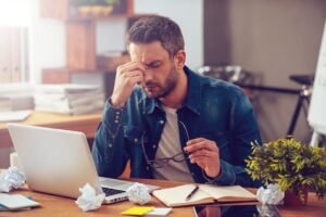 Stressed person sitting at a desk with a laptop and crumpled paper