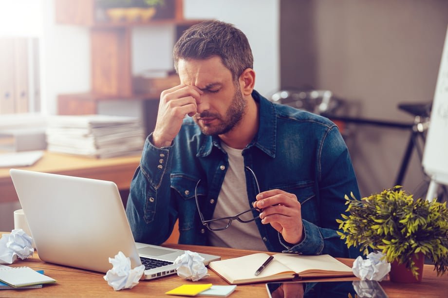 Stressed person sitting at a desk with a laptop and crumpled paper