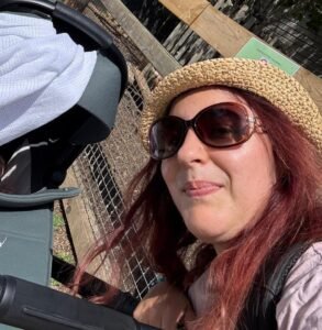 Parent outdoors beside a pram on a sunny day