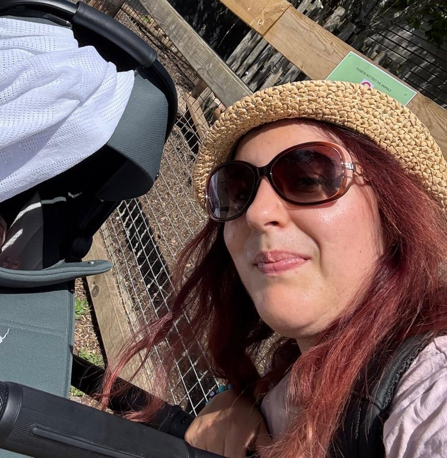 Parent outdoors beside a pram on a sunny day