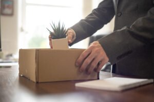 Man packing his desk into a box. He is holding a cactus.