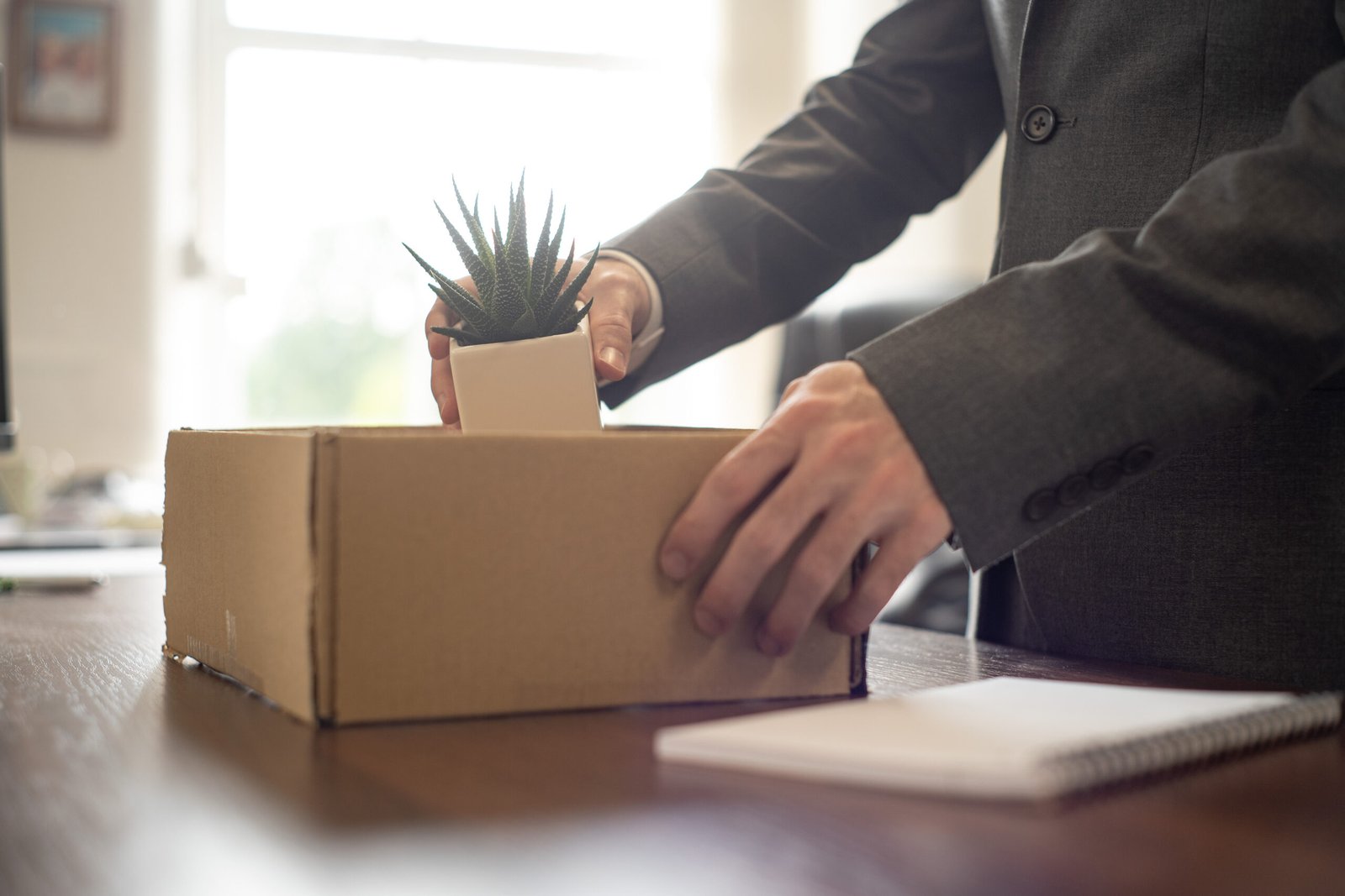 Man packing his desk into a box. He is holding a cactus.