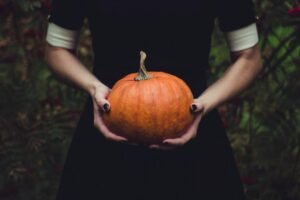 Featured image for this blog post. It is a woman holding a pumpkin. She is wearing a black dress with white sleeves poking out underneath. It looks distinctly autumnal.